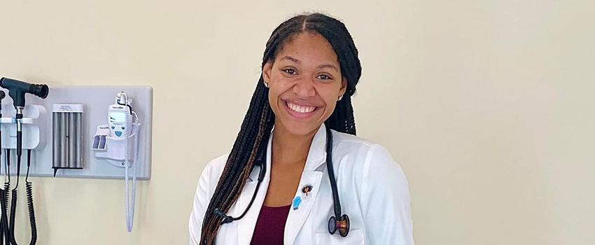 Physician Assistant Studies student in white coat with stethoscope in exam room.