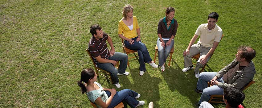 A group of people sitting in chairs in a circle outside talking.