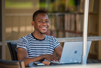 student Sitting at table with laptop smiling.