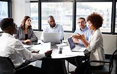 Woman talking at table with group working on laptops.